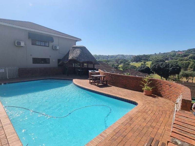 Outdoor pool area featuring a swimming pool, brick paving, a thatch lapa, and a brick retaining wall with scenic views.