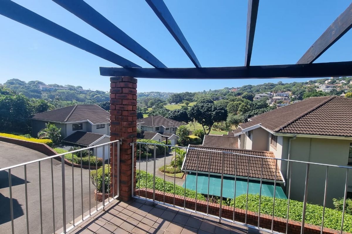 An elevated balcony featuring a timber pergola, brick pillar, and metal balustrade, offering expansive views over the surrounding residential estate.