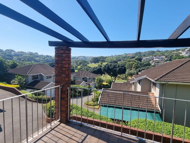 An elevated balcony featuring a timber pergola, brick pillar, and metal balustrade, offering expansive views over the surrounding residential estate.
