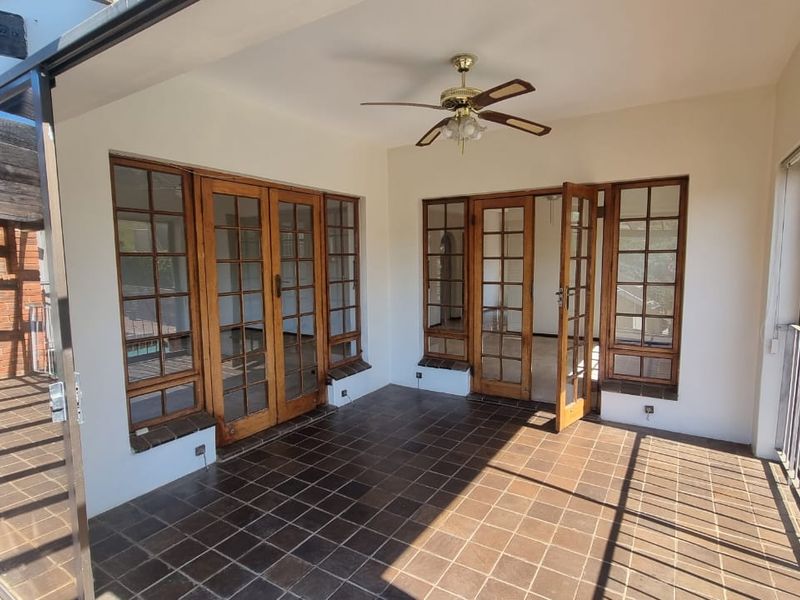 A spacious covered patio featuring tiled flooring, a ceiling fan, and multiple timber-framed glass doors providing seamless access to the interior living spaces.