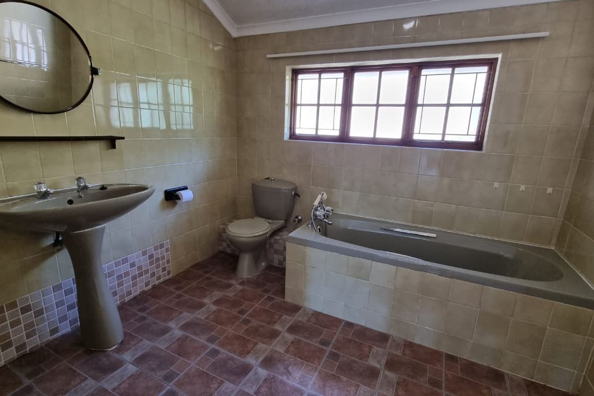 A spacious bathroom featuring a built-in bathtub, pedestal basin, and toilet, finished with neutral wall tiles and patterned floor tiles.