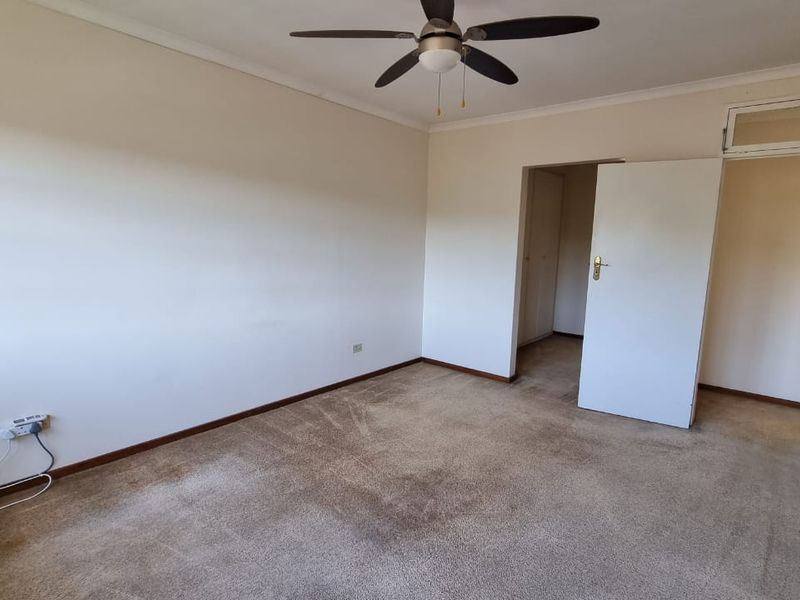 A spacious, empty bedroom featuring neutral walls, carpeted flooring, a ceiling fan, and built-in storage cupboards.