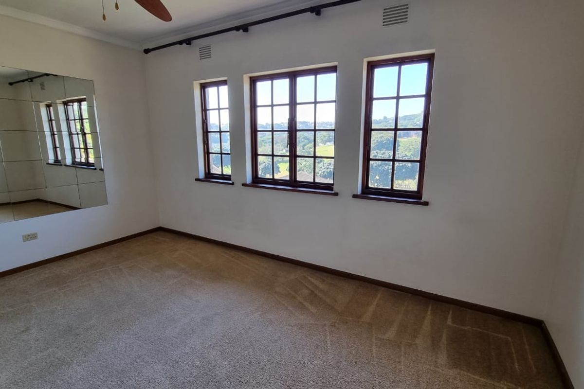 An empty bedroom featuring a large mirrored wall, ceiling fan, and timber-framed windows with views, finished with neutral carpeting.