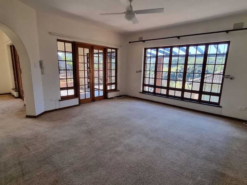 Spacious, empty living room featuring large timber-framed windows, an archway leading to an adjacent area, and a ceiling fan.