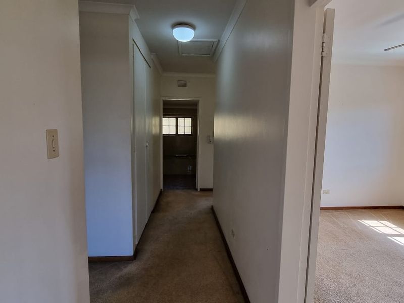 A vacant hallway featuring built-in storage cupboards, carpeted flooring, and access to adjacent rooms, showing signs of wear and dated finishes.