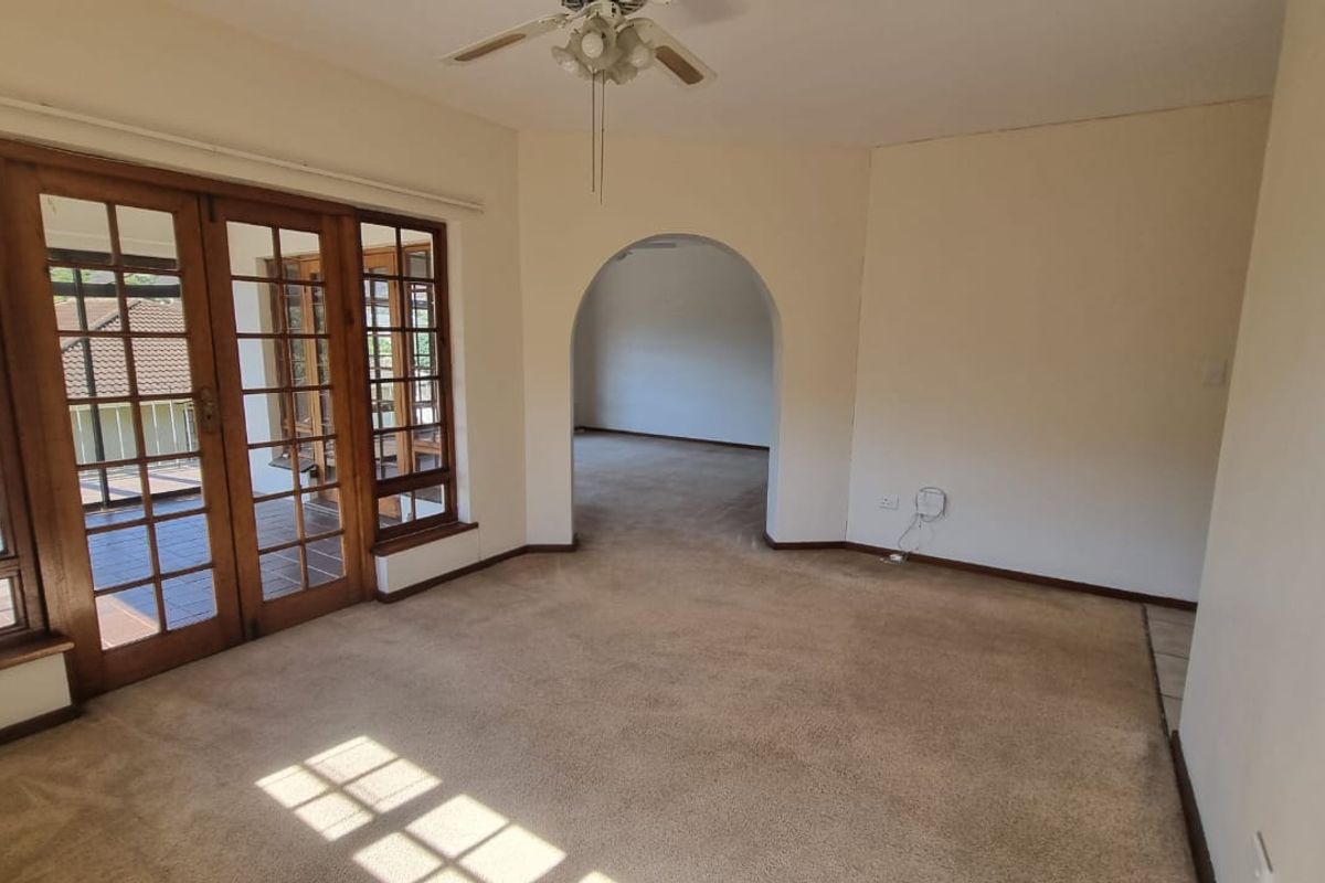 Spacious living area featuring carpeted flooring, a ceiling fan, and large wooden-framed glass doors leading to an outdoor space.