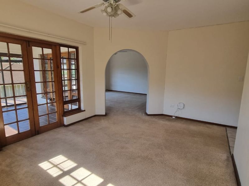 Spacious living area featuring carpeted flooring, a ceiling fan, and large wooden-framed glass doors leading to an outdoor space.