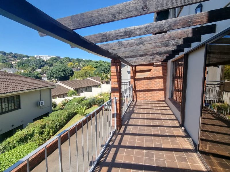 A spacious balcony featuring a timber pergola, brick pillars, and tiled flooring, offering an elevated outdoor space with views of the surrounding residential area.
