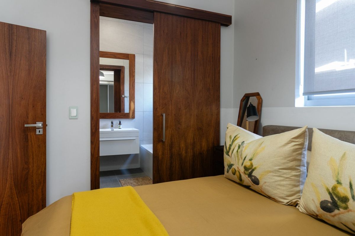 A well-maintained bedroom featuring a sliding wooden door leading to an en-suite bathroom with a modern vanity and mirror.