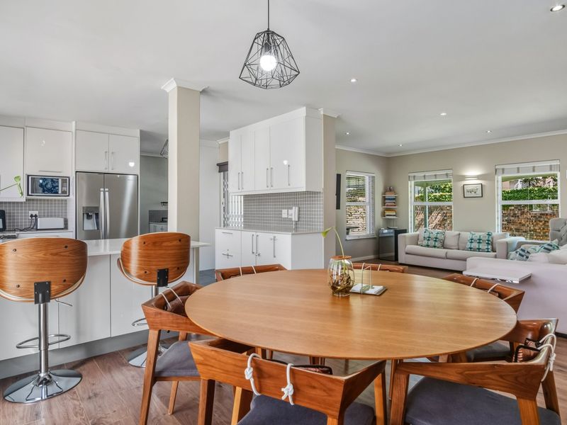 A bright open-plan living and kitchen area featuring modern white cabinetry, a central kitchen island, and wood-look flooring throughout the space.