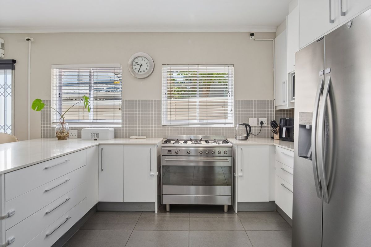 Modern kitchen featuring white cabinetry, quartz countertops, a stainless steel gas stove, and a tiled backsplash with natural light from dual windows.