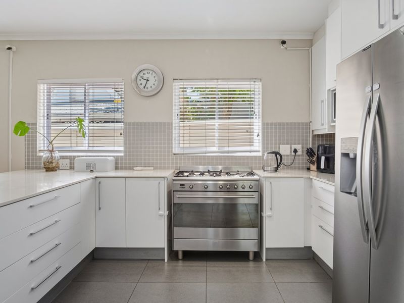 Modern kitchen featuring white cabinetry, quartz countertops, a stainless steel gas stove, and a tiled backsplash with natural light from dual windows.