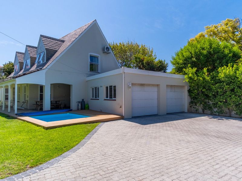 Front exterior view featuring a double garage, paved driveway, covered patio area, and a swimming pool set within a landscaped garden.