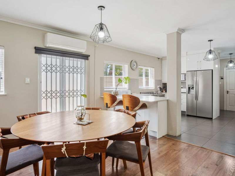 Open-plan living and dining area featuring a modern kitchen with island, tiled and laminate flooring, and split-system air conditioning.