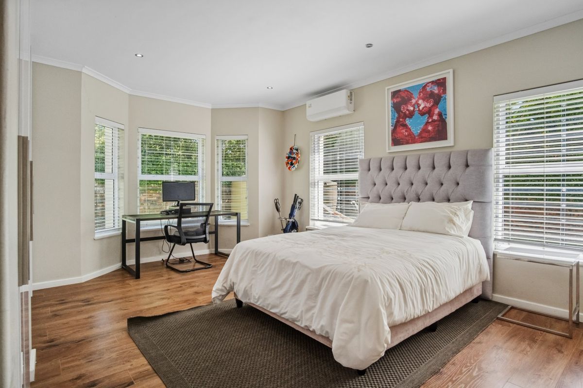 A well-lit bedroom featuring laminate flooring, recessed downlights, a split-system air conditioner, and multiple windows with fitted venetian blinds.