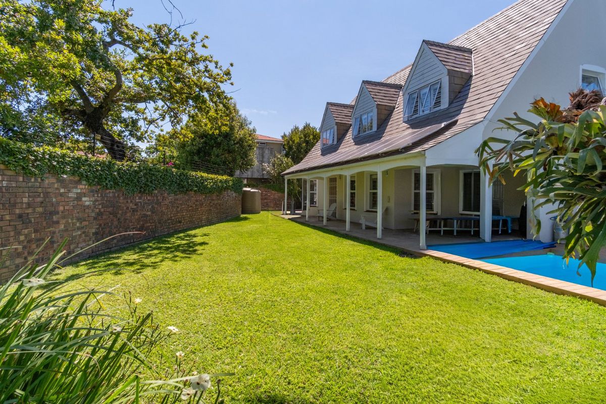 Rear view of the property featuring a well-maintained lawn, a swimming pool, and a covered patio area with dormer windows above.