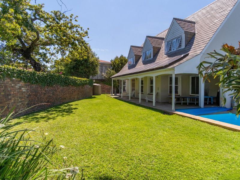 Rear view of the property featuring a well-maintained lawn, a swimming pool, and a covered patio area with dormer windows above.