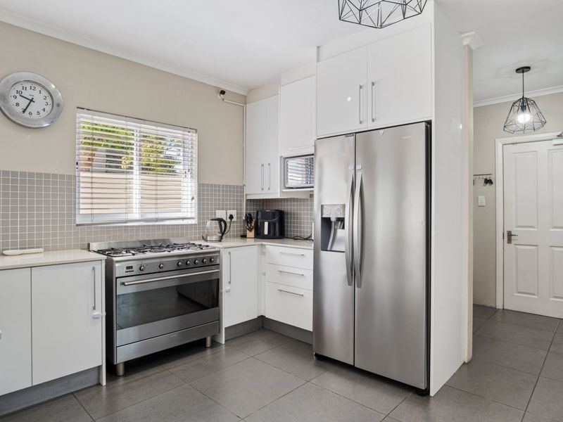 A modern, well-maintained kitchen featuring white cabinetry, a gas stove, tiled backsplash, and sleek floor tiles, offering a clean and functional cooking space.