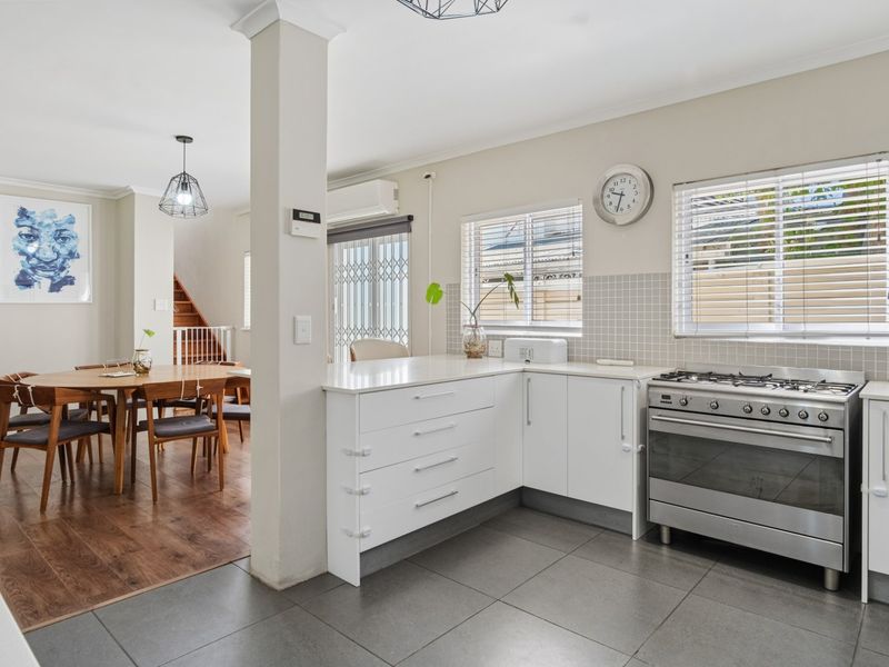 Open-plan kitchen and dining area featuring modern white cabinetry, gas stove, tiled kitchen flooring, and warm laminate flooring in the dining space.