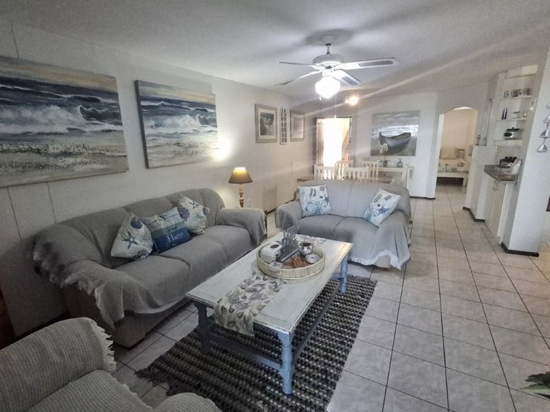 Open-plan living area featuring tiled flooring, a ceiling fan, and an archway leading to the dining space and kitchen area.