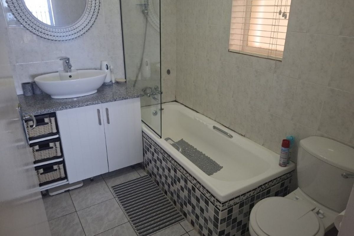 A functional bathroom featuring a vanity with granite countertop, vessel sink, bathtub with glass screen, and tiled finishes throughout.