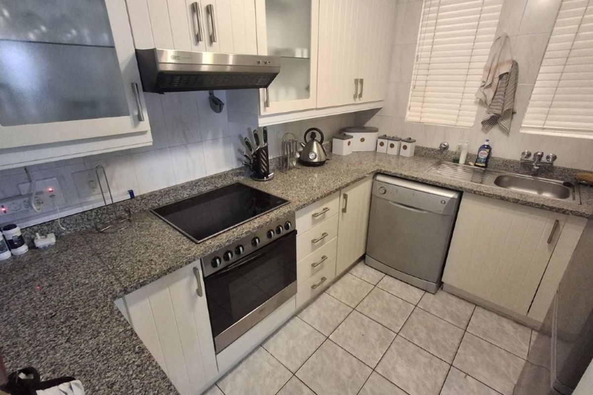 A functional kitchen featuring granite countertops, built-in oven with electric hob, extractor fan, stainless steel sink, and ample fitted cabinetry.