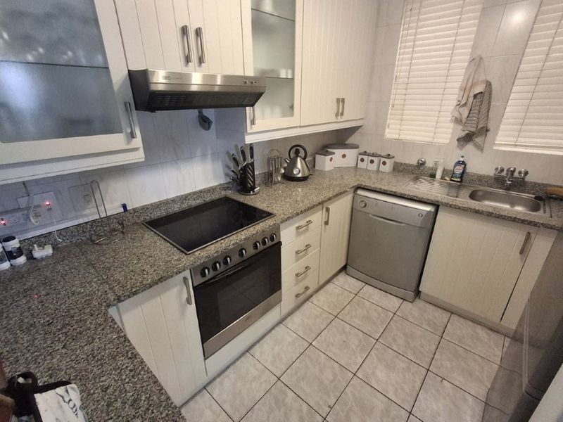 A functional kitchen featuring granite countertops, built-in oven with electric hob, extractor fan, stainless steel sink, and ample fitted cabinetry.