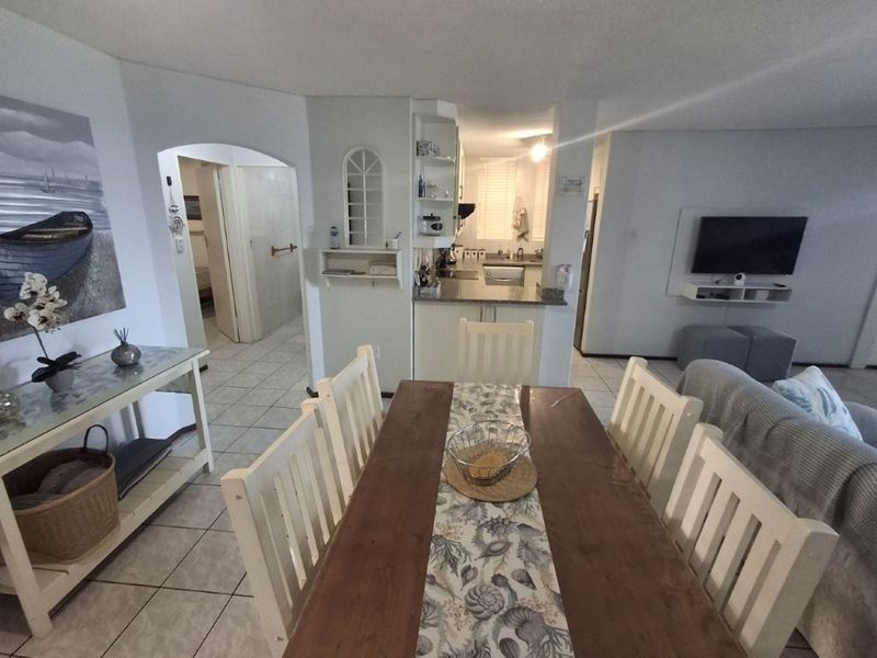 Open-plan living and dining area featuring tiled flooring, an archway leading to the hallway, and a functional kitchen with built-in cabinetry.