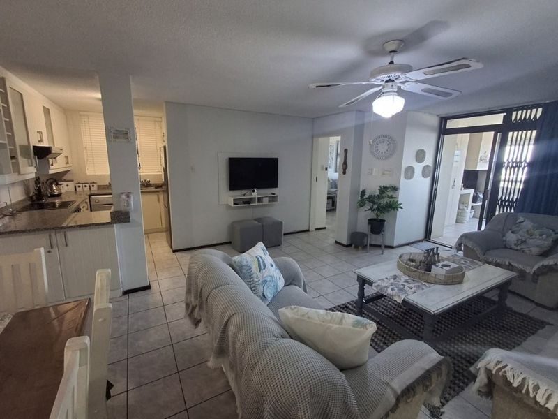 Open-plan living area featuring tiled floors, a ceiling fan, and an adjoining kitchen with granite countertops and ample cabinetry.