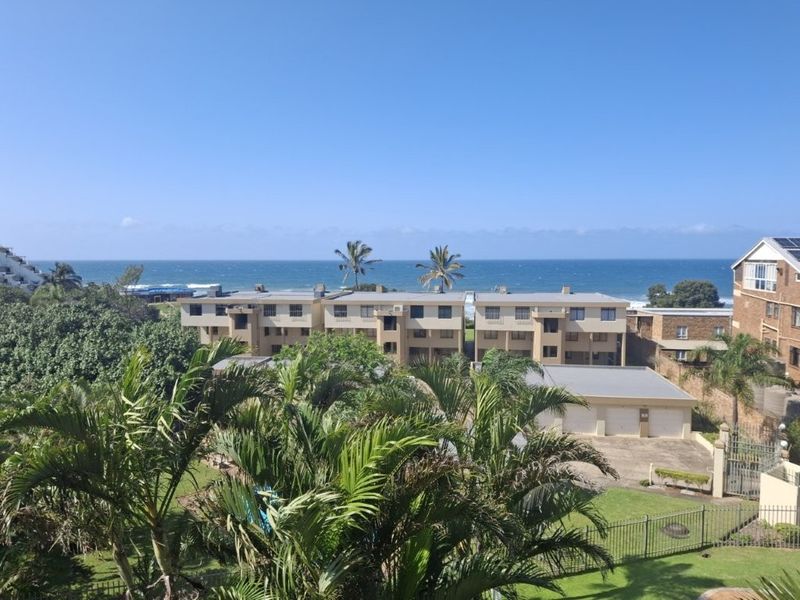 An elevated view overlooking the apartment complex grounds, surrounding greenery, and the ocean horizon.