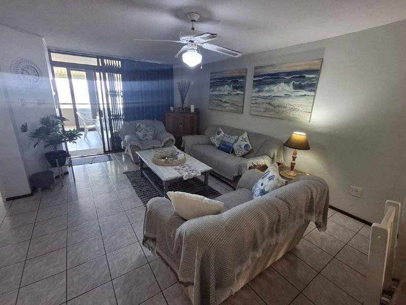 A comfortable living room featuring tiled flooring, a ceiling fan, and a sliding glass door providing access to an outdoor balcony area.
