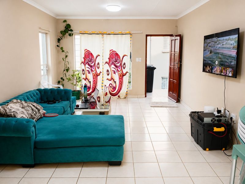 A spacious living room featuring neutral wall tones, tiled flooring, and direct access to an outdoor area through a timber door.