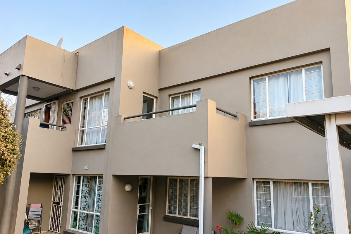 Rear elevation of a multi-story apartment building featuring balconies, aluminium-framed windows, and security gates.