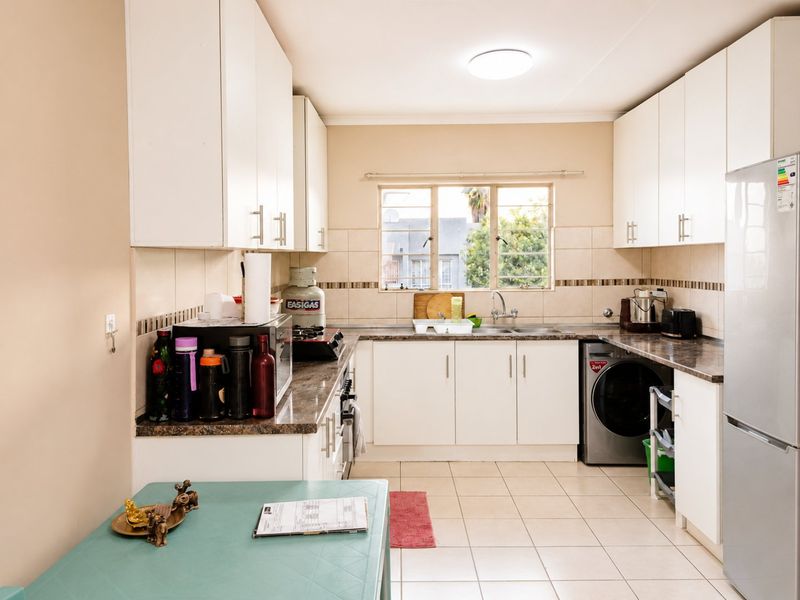 A functional kitchen featuring white cabinetry, laminate countertops, tiled backsplash, and an integrated washing machine, offering a clean and practical workspace.