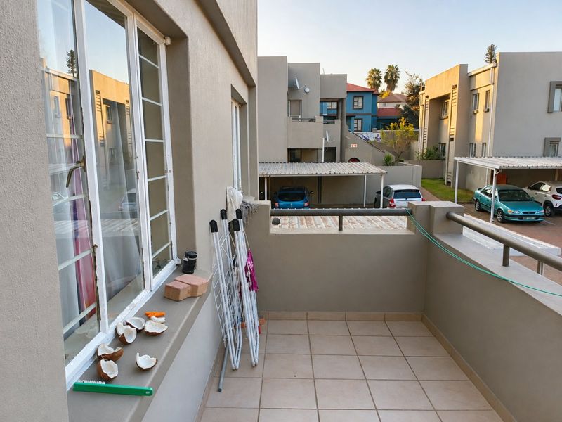 A functional balcony area with tiled flooring and metal balustrade, overlooking the apartment complex parking area.