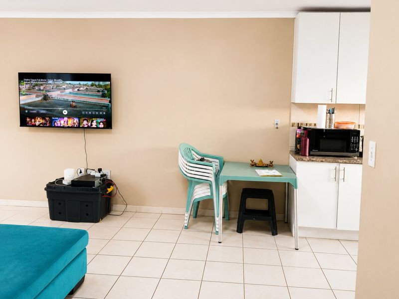 Open-plan living area featuring tiled flooring and a compact kitchen corner with white cabinetry and laminate countertops.