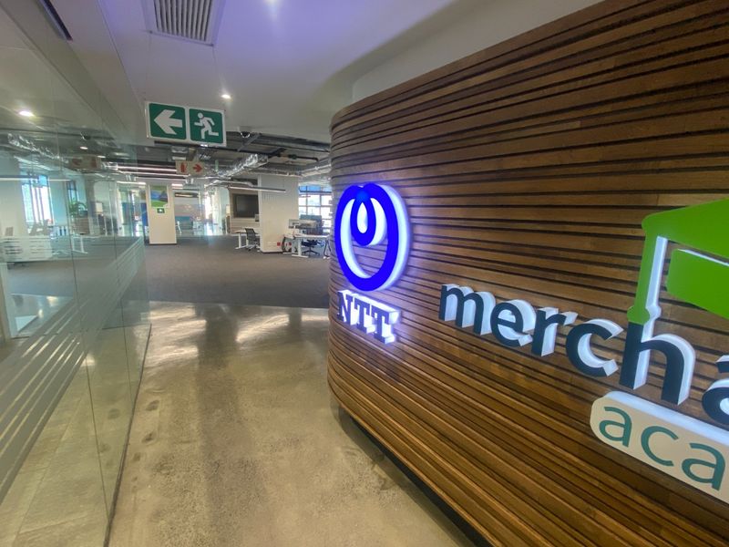 Modern commercial office entrance featuring a curved slatted timber wall with illuminated corporate branding and polished concrete flooring.