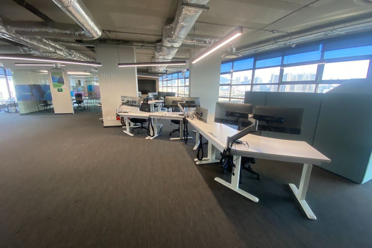 Modern open-plan commercial office space featuring exposed industrial ceilings, large windows with city views, and integrated linear lighting.