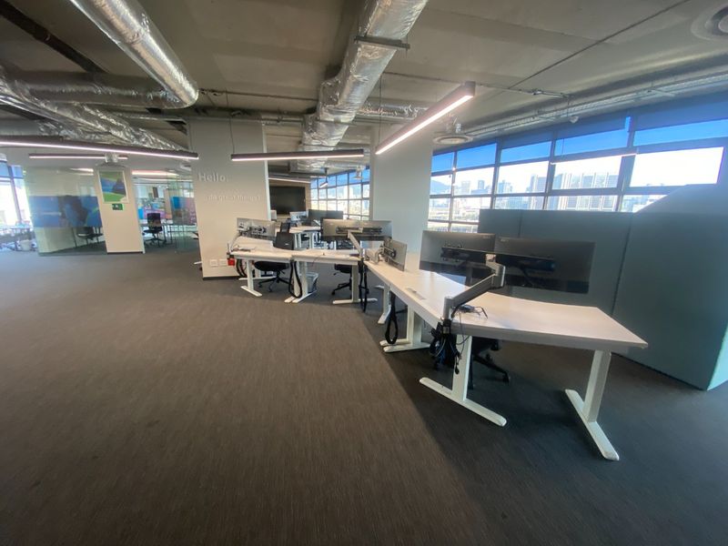 Modern open-plan commercial office space featuring exposed industrial ceilings, large windows with city views, and integrated linear lighting.