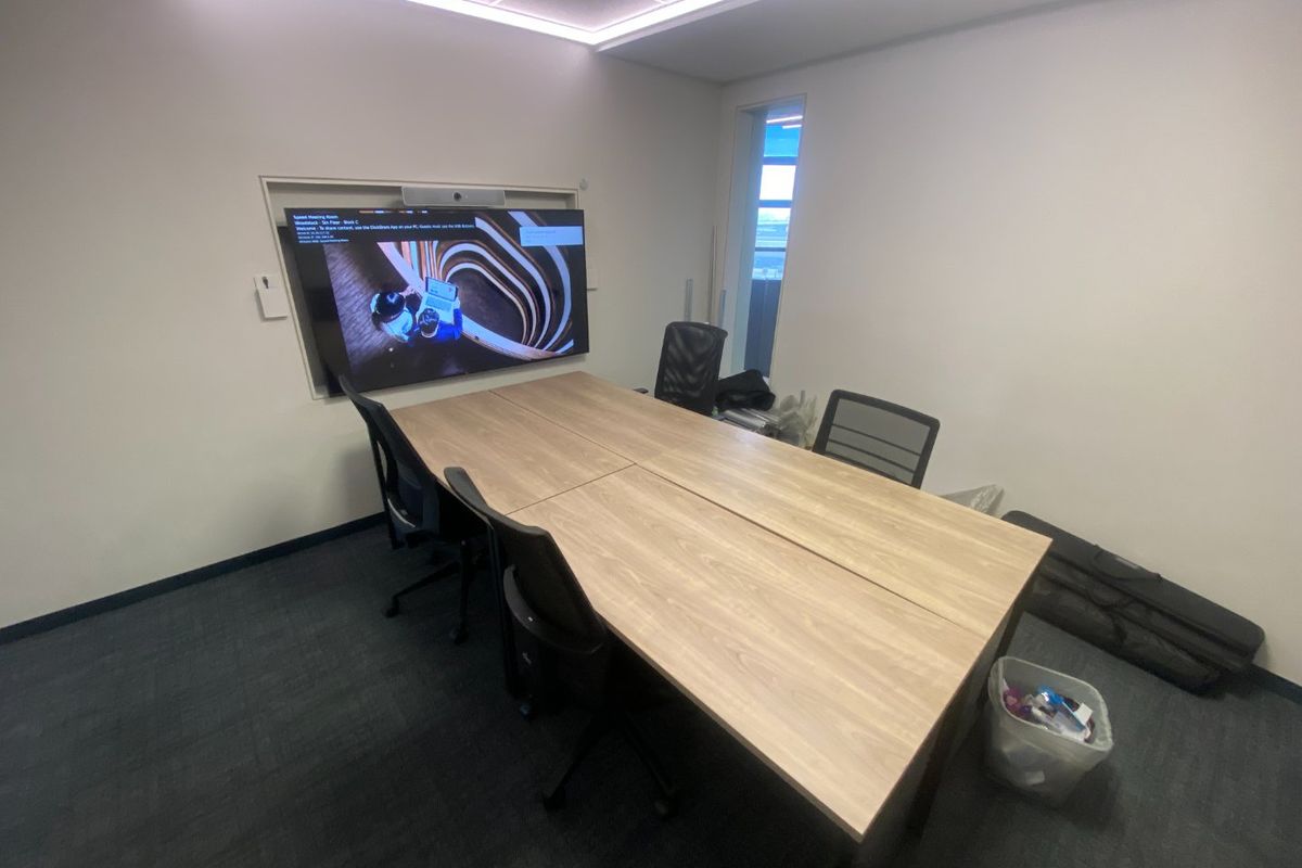 A functional commercial meeting room featuring a large wall-mounted display screen, recessed ceiling lighting, and carpeted flooring.
