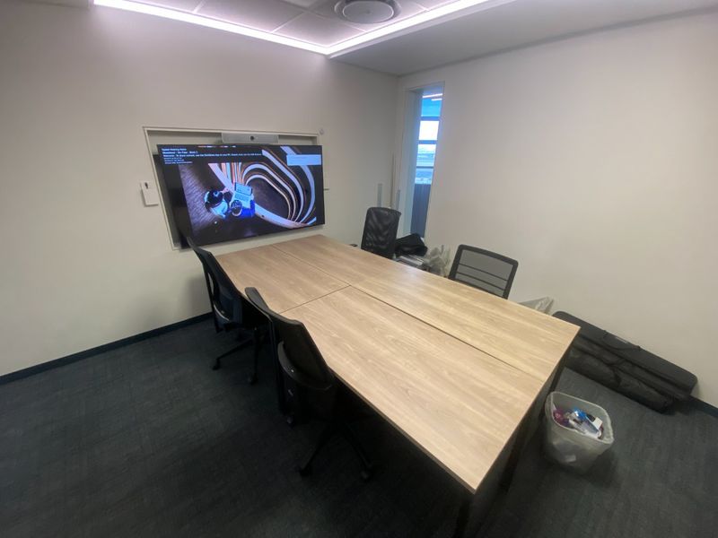 A functional commercial meeting room featuring a large wall-mounted display screen, recessed ceiling lighting, and carpeted flooring.
