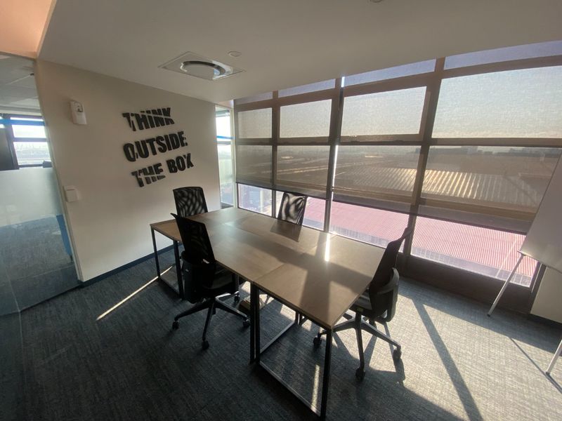 A modern office meeting room featuring large floor-to-ceiling windows with roller blinds, recessed ceiling lighting, and professional carpeted flooring.