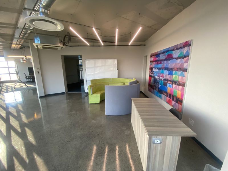 Modern open-plan office space featuring polished concrete floors, exposed industrial ceiling with ducted air conditioning, and contemporary linear lighting fixtures.
