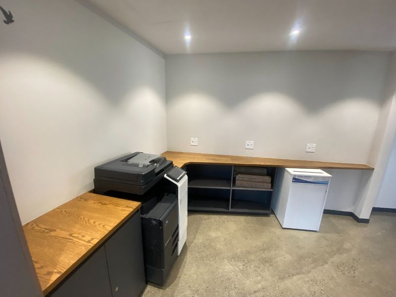 A functional office space featuring a built-in timber desk, integrated storage cabinetry, polished concrete floors, and recessed downlighting.