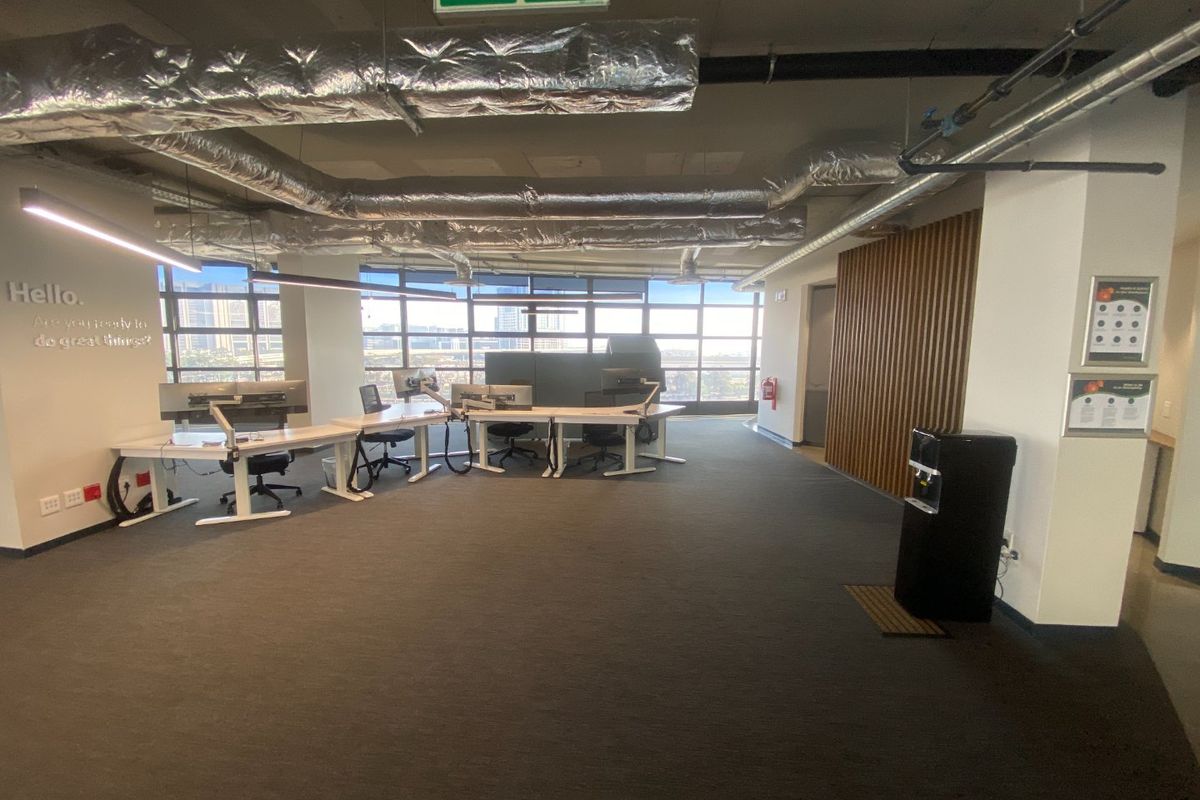 Modern open-plan commercial office space featuring exposed industrial ceiling ducting, large windows with natural light, and contemporary timber wall accents.