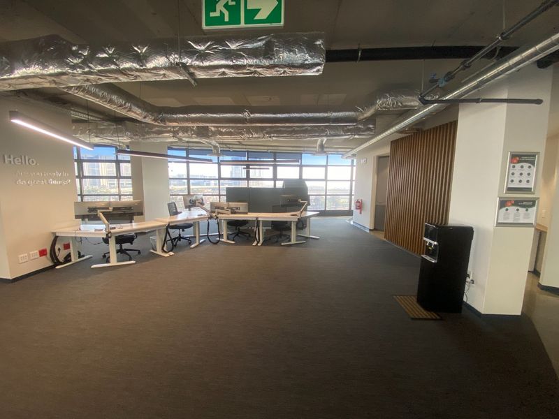 Modern open-plan commercial office space featuring exposed industrial ceiling ducting, large windows with natural light, and contemporary timber wall accents.