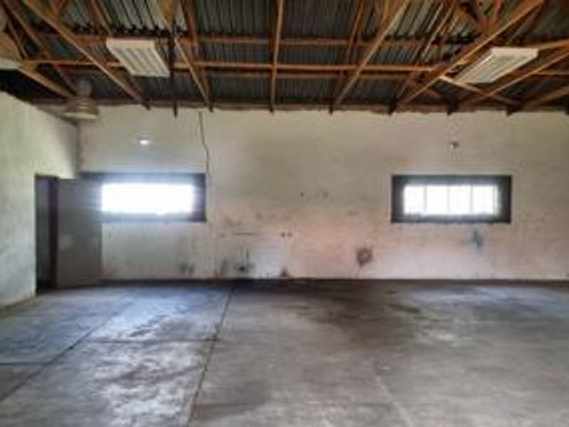 A spacious, empty utility or industrial space featuring exposed timber roof trusses, concrete flooring, and functional lighting, suitable for various commercial storage or workshop uses.