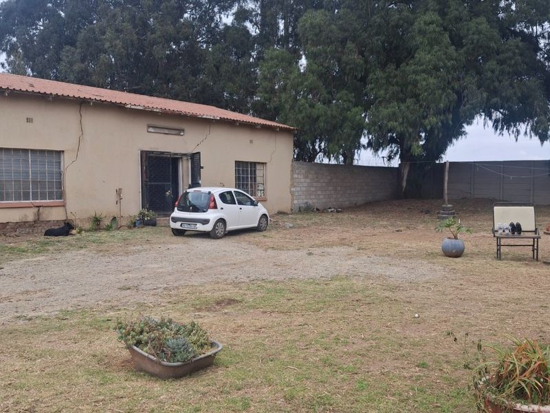 Rear exterior view of a commercial property featuring a large yard, perimeter wall, and building structure with visible maintenance requirements.