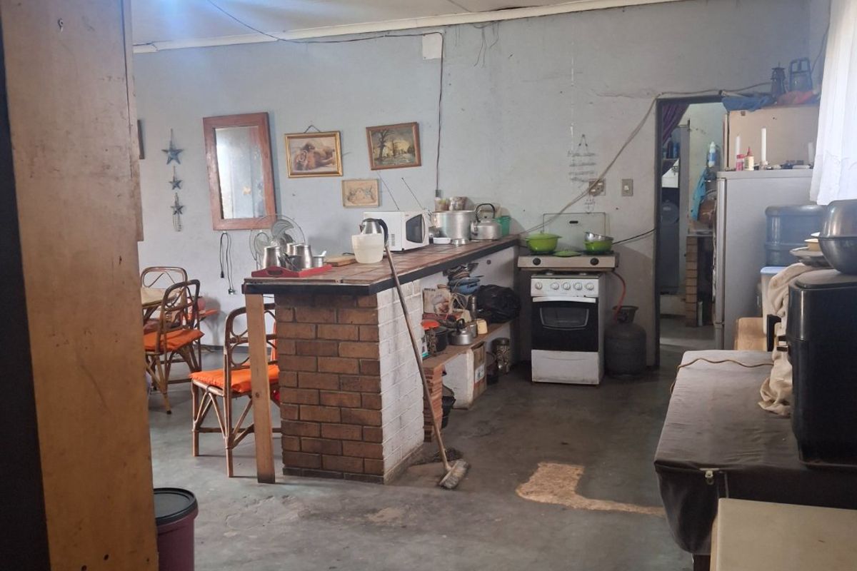 A dated kitchen area featuring a brick breakfast bar, freestanding oven, and ceiling fan, requiring significant cosmetic updates and maintenance to the walls and flooring.