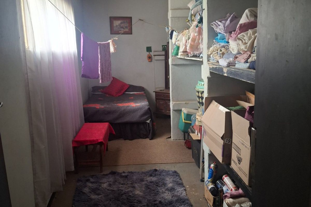 A small bedroom featuring built-in shelving units and a window with curtains, requiring cosmetic updates and maintenance to improve the overall condition.